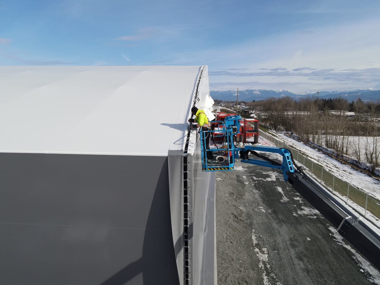 Worker completing fabric building installation detail work from a boom lift.